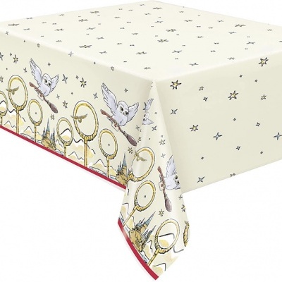 Toalha de mesa bege com estampado de estrelas e borda com desenhos de óculos, varinhas, pombos e castelos