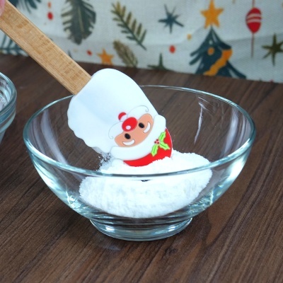 Espátula de silicone com desenho de Pai Natal dentro de taça de vidro com pó branco