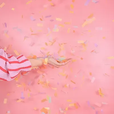 Braço com manga vermelha às riscas brancas e confetis coloridos sobre fundo rosa