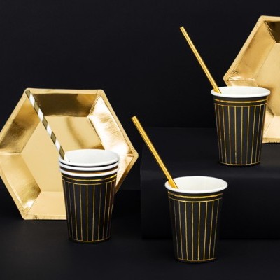 Copos pretos com riscas douradas, palhinhas e pratos hexagonais dourados