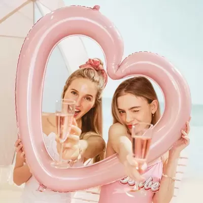 Duas mulheres com balão insuflável em forma de coração cor-de-rosa e taças de bebida cor-de-rosa na praia
