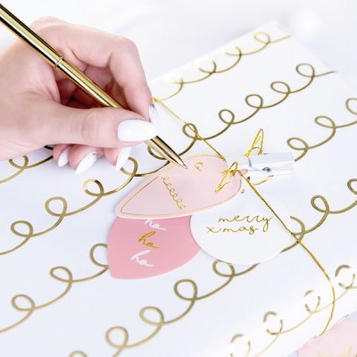 Mão feminina escrevendo em etiquetas de presente sobre papel de embrulho branco com padrão dourado