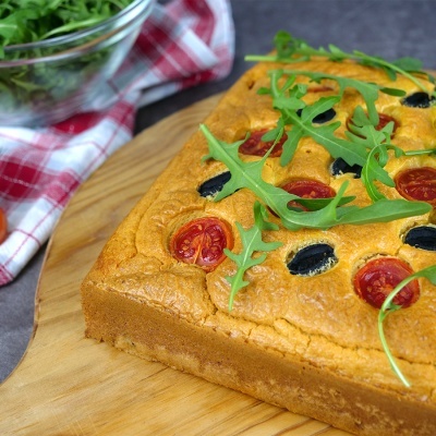 Focaccia com tomate, azeitonas e rúcula numa tábua de madeira