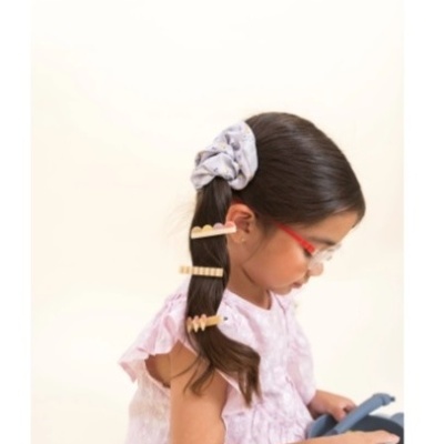 Criança com acessórios de cabelo e óculos vermelhos a olhar para baixo