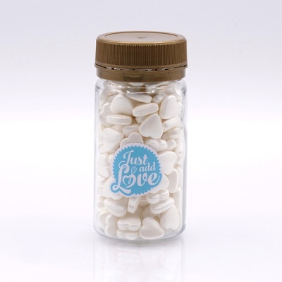 Frasco transparente com pastilhas brancas em forma de coração e etiqueta azul 'Just add Love'