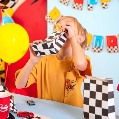 Criança segurando objeto de papelão com padrão preto e branco, mesa com brinquedos e decoração colorida ao fundo.