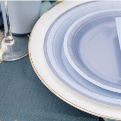 Conjunto de pratos descartáveis azuis sobre prato branco com borda dourada numa mesa azul