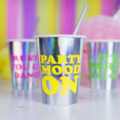 Três copos metálicos decorados com texto colorido em ambiente festivo