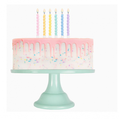 Bolo redondo com glacê rosa a escorrer, cinco velas coloridas acesas, suporte de bolo verde água