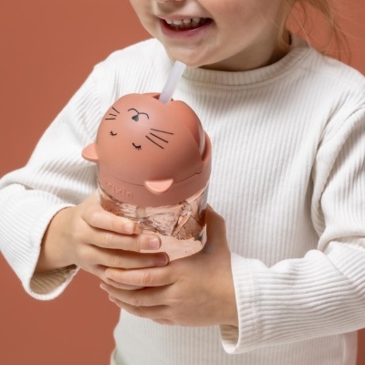 Copo infantil com tampa de gato cor de rosa e palhinha, segurado por criança com camisola branca