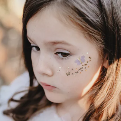 Menina com faixa de cabelo rosa e adesivos brilhantes na face