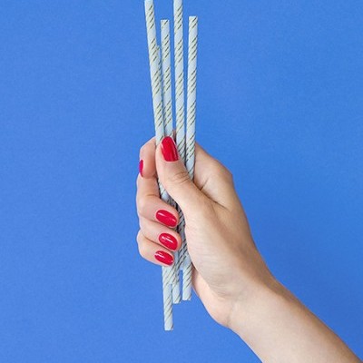 Mão a segurar palhinhas brancas com riscas verdes, fundo azul