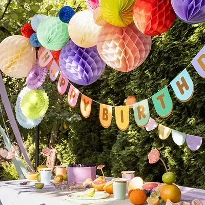 Decoração de festa com lanternas de papel coloridas e faixa HAPPY BIRTHDAY sobre mesa posta ao ar livre