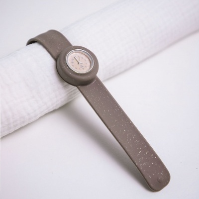 Relógio com bracelete castanha e padrão de manchas brancas sobre tecido branco