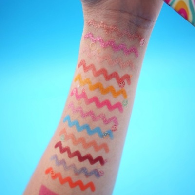 Braço com amostras coloridas de maquilhagem em padrão ondulado sobre fundo azul