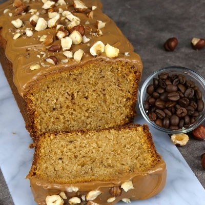 Bolo com cobertura castanha e avelãs ao lado de taça com grãos de café