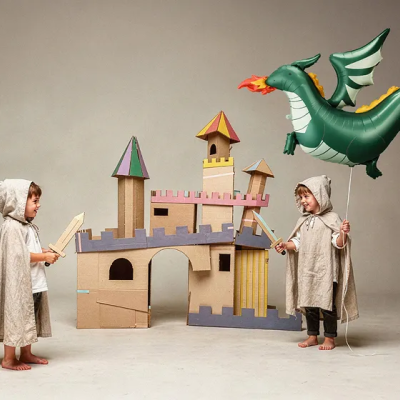 Crianças com capas e espadas de madeira brincando com castelo de cartão e balão de dragão inflável