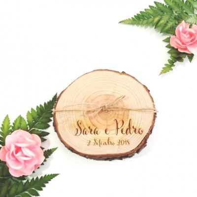 Disco de madeira gravado com nomes e data rodeado por folhas e flores cor de rosa