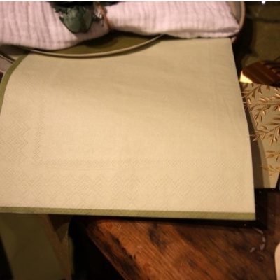 Toalha de mesa verde clara com bordas e textura geométrica sobre mesa de madeira escura, pano rosa ao fundo