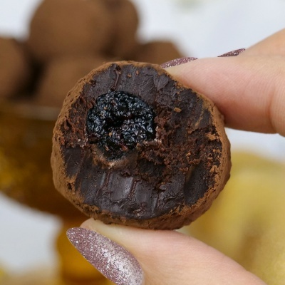 Trufa de chocolate castanha com recheio escuro segurada entre dedos.