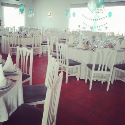 Sala de evento com mesas e cadeiras brancas decoradas com balões azuis e brancos