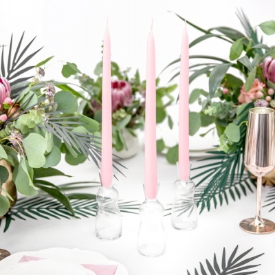 Mesa decorada com castiçais de vidro, velas rosas, copos metálicos cor de cobre e arranjos florais em vasos dourados sobre toalha branca