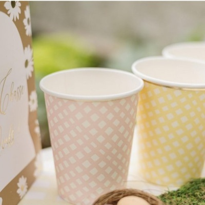 Copos de papel rosa e amarelo com padrão quadriculado branco em mesa