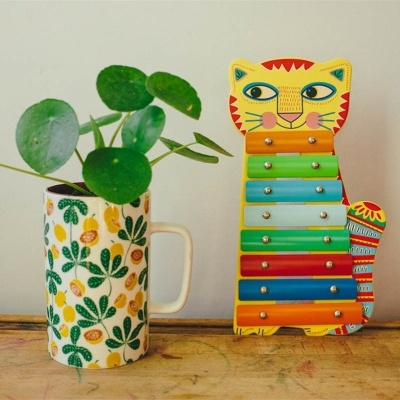 Planta em jarro branco decorado e xilofone em forma de gato colorido sobre mesa de madeira