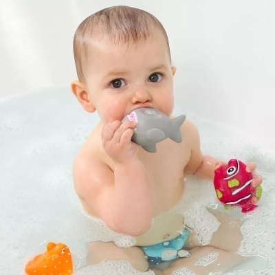 Bebé na banheira com brinquedos de banho coloridos de golfinho e peixe.