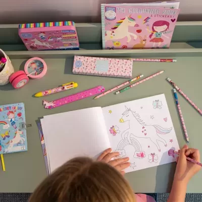 Criança a colorir desenho de unicórnio com material escolar colorido à volta