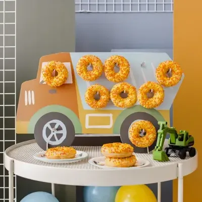 Mesa com rosquinhas amarelas crocantes, suporte de camião de cartão e brinquedo de trator verde.