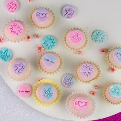 Doces decorativos em tons pastel com desenhos de unicórnios, estrelas, corações e arco-íris sobre base branca