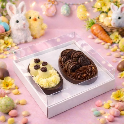 Caixa com dois ovos de chocolate decorados em cenário de Páscoa colorido.