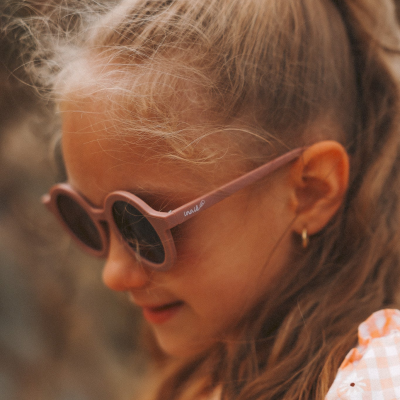 Criança com óculos de sol rosas redondos e cabelo loiro com fita rosa