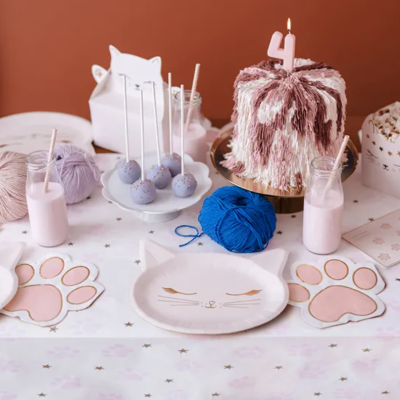 Mesa de festa infantil decorada com tema gatinho, bolo, pratos, guardanapos, bolas de lã e copos