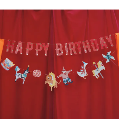 Decoração de festa com faixas HAPPY BIRTHDAY e figuras coloridas penduradas em fundo vermelho e laranja