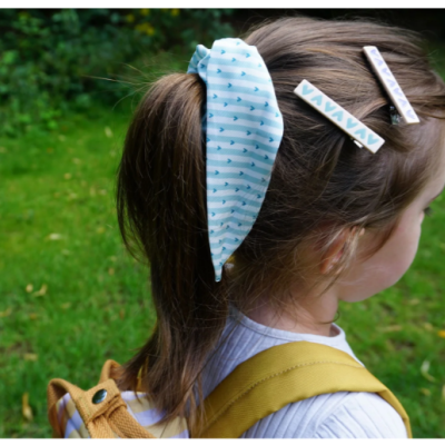 Cabelo de criança com acessórios azuis e brancos num fundo de relvado verde