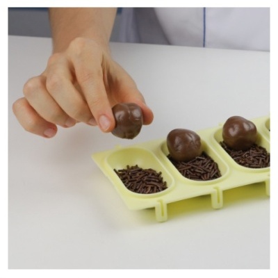 Bola de chocolate sendo colocada num tabuleiro amarelo com confeitos de chocolate.