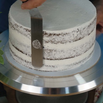 Bolo de chocolate com cobertura branca sendo alisado com espátula metálica