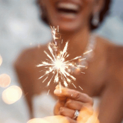 Mulher segura fogo de artifício aceso com luzes desfocadas ao fundo