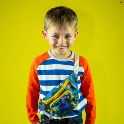 Menino com camisola riscada e bolsa de dinossauros em fundo amarelo