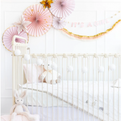 Berço branco com almofadas e decorações de festa em rosa e dourado