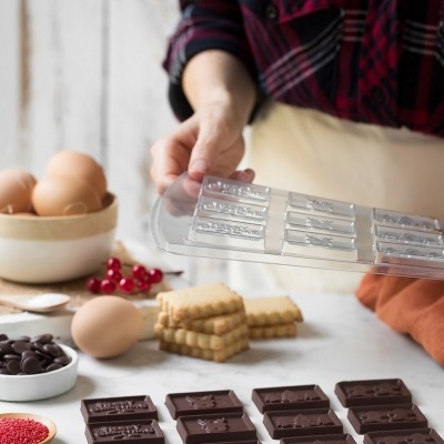 Barras de chocolate preto moldadas sobre uma mesa com moldes plásticos e ingredientes de confeitaria