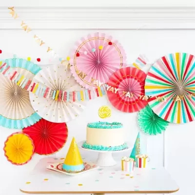 Decoração de festa colorida com flores de papel, bolo e acessórios.