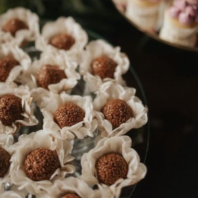Docinhos brigadeiros em forminhas brancas sobre pratos escuros