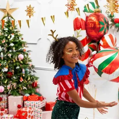 Criança vestida com roupa festiva de Natal perto de árvore e presentes