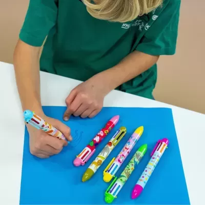 Criança a desenhar com canetas multicoloridas em papel azul numa mesa branca