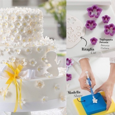 Bolo branco com decoração de flores pequenas e ferramentas para cortar e modelar flores de pasta de açúcar.