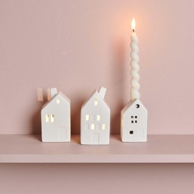 Três casas decorativas brancas com luzes e castiçal com vela