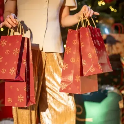 Mulher segurando sacolas de papel vermelhas com motivos natalinos dourados